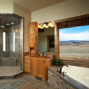 Exemple d'une grande salle de bain principale montagne avec un placard à porte affleurante, des portes de placard en bois brun, une baignoire d'angle, une douche d'angle, un carrelage marron, un carrelage gris, un carrelage de pierre, un mur beige, un sol en carrelage de porcelaine, un lavabo posé et un plan de toilette en cuivre.