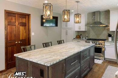 Eat-in kitchen - large industrial l-shaped medium tone wood floor and brown floor eat-in kitchen idea in Other with an undermount sink, recessed-panel cabinets, white cabinets, granite countertops, gray backsplash, porcelain backsplash, stainless steel appliances, an island and multicolored countertops