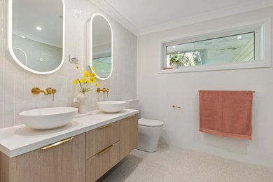 Photo of a large beach style 3/4 bathroom in Sydney with light wood cabinets, an open shower, a two-piece toilet, white tile, white walls, a vessel sink, multi-coloured floor, an open shower, white benchtops, a niche, a double vanity and a floating vanity.