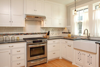 Example of a classic enclosed kitchen design in Minneapolis with a farmhouse sink, shaker cabinets, white cabinets, multicolored backsplash and stainless steel appliances