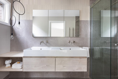 This is an example of a small contemporary 3/4 bathroom in Melbourne with beaded inset cabinets, light wood cabinets, an alcove shower, a bidet, beige tile, porcelain tile, grey walls, porcelain floors, an integrated sink, grey floor, a sliding shower screen, white benchtops, a double vanity and a floating vanity.