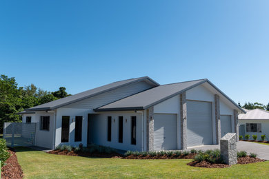 Imagen de fachada de casa gris y gris actual grande de una planta con revestimiento de hormigón, tejado a dos aguas, tejado de metal y panel y listón