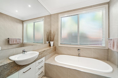 Contemporary bathroom in Melbourne with furniture-like cabinets, white cabinets, a drop-in tub, beige tile, an integrated sink and granite benchtops.
