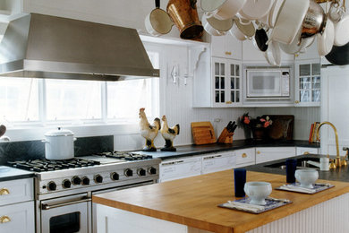 Kitchen pantry - coastal u-shaped light wood floor kitchen pantry idea in New York with a single-bowl sink, recessed-panel cabinets, white cabinets, soapstone countertops, white backsplash, stainless steel appliances and an island