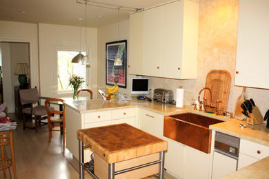 Small transitional l-shaped light wood floor eat-in kitchen photo in San Francisco with a farmhouse sink, flat-panel cabinets, white cabinets, limestone countertops, beige backsplash, stone tile backsplash, stainless steel appliances and an island