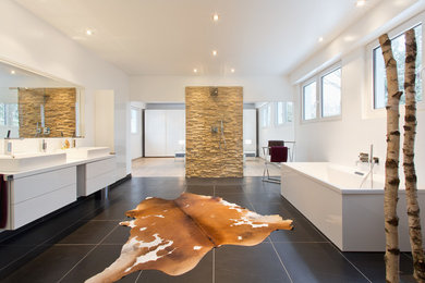 Geräumiges Modernes Badezimmer En Suite mit flächenbündigen Schrankfronten, weißen Schränken, bodengleicher Dusche, Wandtoilette, weißer Wandfarbe, Schieferboden, Aufsatzwaschbecken, schwarzem Boden, offener Dusche und weißer Waschtischplatte in Köln