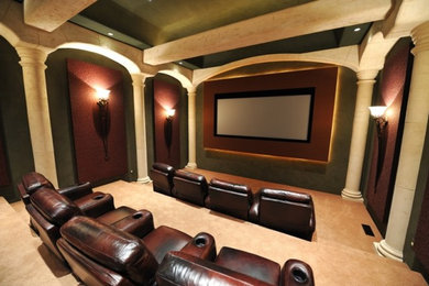 This is an example of a large mediterranean enclosed home theatre in New York with green walls, carpet, a projector screen and beige floor.