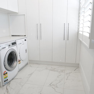 メルボルンの中サイズのコンテンポラリースタイルのおしゃれなランドリークローゼット (ドロップインシンク、フラットパネル扉のキャビネット、白いキャビネット、ライムストーンカウンター、白い壁、大理石の床、左右配置の洗濯機・乾燥機、白い床) の写真