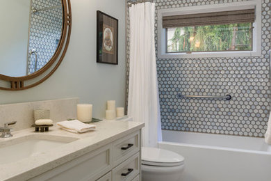 This is an example of a mid-sized transitional bathroom in Seattle with recessed-panel cabinets, grey cabinets, an alcove tub, a shower/bathtub combo, a one-piece toilet, gray tile, porcelain tile, grey walls, porcelain floors, an undermount sink, engineered quartz benchtops, beige floor and a shower curtain.