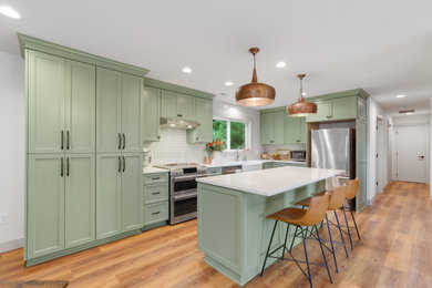 Inspiration for a large craftsman u-shaped vinyl floor and brown floor eat-in kitchen remodel in Portland with a farmhouse sink, recessed-panel cabinets, green cabinets, quartz countertops, white backsplash, ceramic backsplash, stainless steel appliances, an island and white countertops