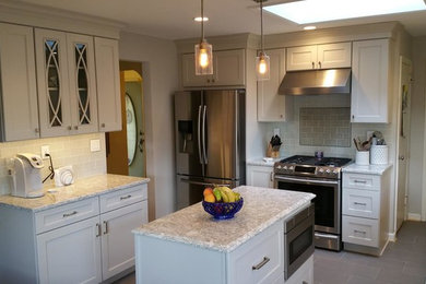 Small elegant l-shaped ceramic tile enclosed kitchen photo in New York with a farmhouse sink, shaker cabinets, white cabinets, granite countertops, gray backsplash, ceramic backsplash, stainless steel appliances and an island