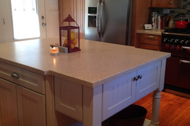 Example of a mid-sized mountain style l-shaped medium tone wood floor open concept kitchen design in Other with a farmhouse sink, beaded inset cabinets, light wood cabinets, solid surface countertops, beige backsplash, glass tile backsplash, stainless steel appliances and an island