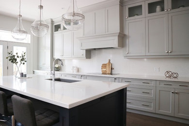 Photo of a large transitional galley open plan kitchen in Toronto with an undermount sink, shaker cabinets, grey cabinets, quartz benchtops, white splashback, stone slab splashback, stainless steel appliances, medium hardwood floors, with island, brown floor and white benchtop.