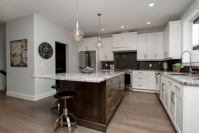 Inspiration for a large contemporary l-shaped light wood floor open concept kitchen remodel in Vancouver with a drop-in sink, raised-panel cabinets, white cabinets, granite countertops, black backsplash, subway tile backsplash, stainless steel appliances and an island