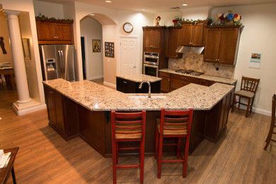 Inspiration for a large timeless porcelain tile and brown floor kitchen remodel in Other with an undermount sink, recessed-panel cabinets, medium tone wood cabinets, quartz countertops, beige backsplash, travertine backsplash, stainless steel appliances, two islands and beige countertops