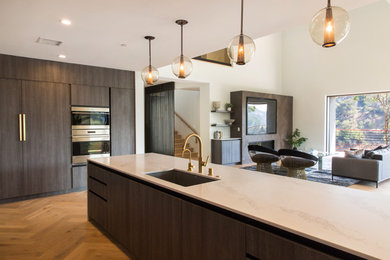 Inspiration for an expansive modern u-shaped open plan kitchen in Los Angeles with an undermount sink, flat-panel cabinets, dark wood cabinets, marble benchtops, white splashback, marble splashback, stainless steel appliances, light hardwood floors, with island and white benchtop.