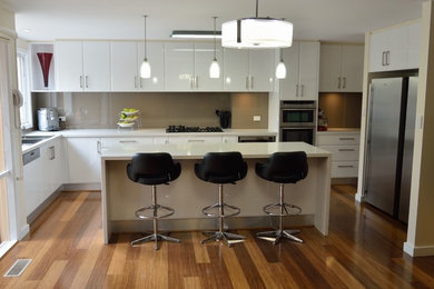 Inspiration for a large modern l-shaped eat-in kitchen in Melbourne with a double-bowl sink, open cabinets, white cabinets, granite benchtops, brown splashback, glass sheet splashback, stainless steel appliances, bamboo floors and with island.