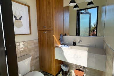 Example of a mid-sized beach style beige tile and porcelain tile mosaic tile floor and multicolored floor toilet room design in Sacramento with a two-piece toilet, beige walls, an integrated sink, marble countertops, white countertops and a floating vanity