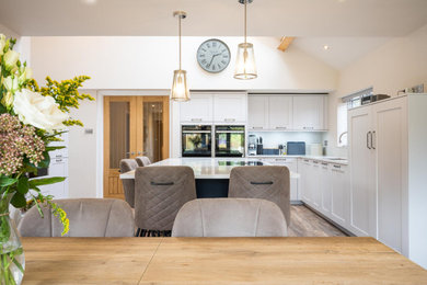 Inspiration for a large contemporary open plan kitchen in Kent with white cabinets, quartzite benchtops, black appliances, with island and white benchtop.