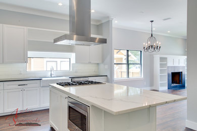 Elegant medium tone wood floor and brown floor eat-in kitchen photo in Houston with a farmhouse sink, shaker cabinets, white cabinets, quartz countertops, white backsplash, subway tile backsplash, stainless steel appliances and an island