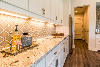 Photo of a mid-sized transitional u-shaped eat-in kitchen in Houston with a farmhouse sink, shaker cabinets, white cabinets, granite benchtops, grey splashback, ceramic splashback, stainless steel appliances, vinyl floors, with island and grey floor.