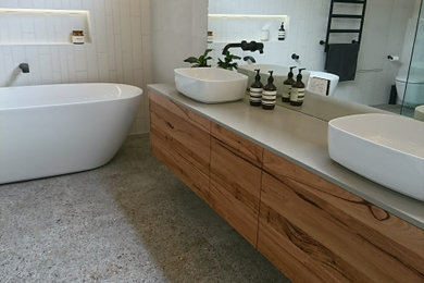 Inspiration for a large modern bathroom in Melbourne with flat-panel cabinets, medium wood cabinets, a freestanding bath, a one-piece toilet, white tiles, ceramic tiles, white walls, terrazzo flooring, a vessel sink, engineered stone worktops, grey floors, a hinged door, a wall niche, double sinks, a floating vanity unit, a vaulted ceiling and grey worktops.
