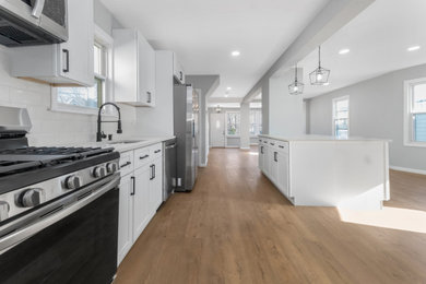 Mid-sized trendy single-wall vinyl floor and brown floor eat-in kitchen photo with an undermount sink, shaker cabinets, white cabinets, quartzite countertops, white backsplash, subway tile backsplash, stainless steel appliances, an island and white countertops