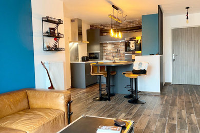 Cette photo montre une salle de séjour industrielle de taille moyenne et ouverte avec un bar de salon, un mur bleu, parquet foncé, aucune cheminée, un téléviseur fixé au mur et un sol marron.