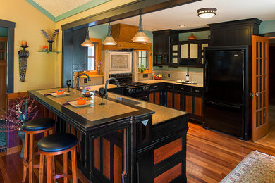 Example of a large arts and crafts u-shaped medium tone wood floor and brown floor enclosed kitchen design in Boston with an undermount sink, recessed-panel cabinets, black cabinets, quartz countertops, black appliances, a peninsula and brown countertops
