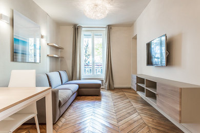 Exemple d'une salle de séjour tendance de taille moyenne et fermée avec un mur beige, un sol en bois brun, un téléviseur fixé au mur et un sol beige.