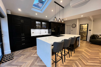 Design ideas for a medium sized contemporary single-wall kitchen/diner in Cheshire with a built-in sink, shaker cabinets, black cabinets, quartz worktops, black appliances, dark hardwood flooring, an island, brown floors, white worktops, a vaulted ceiling and feature lighting.