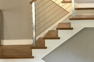 Immagine di una grande scala a "L" minimalista con pedata in legno, alzata in legno e parapetto in cavi
