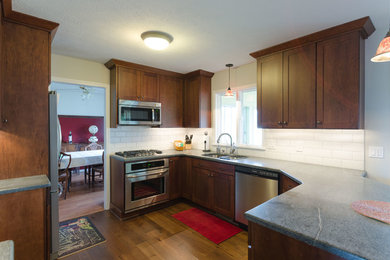 Inspiration for a mid-sized transitional l-shaped medium tone wood floor eat-in kitchen remodel in New York with an undermount sink, recessed-panel cabinets, medium tone wood cabinets, soapstone countertops, white backsplash, ceramic backsplash, stainless steel appliances and a peninsula