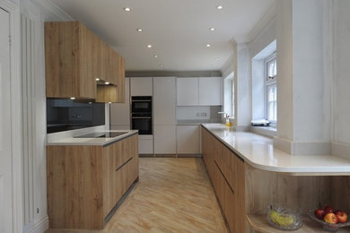 Medium sized galley enclosed kitchen in Kent with a submerged sink, flat-panel cabinets, light wood cabinets, quartz worktops, grey splashback, mirror splashback, black appliances, light hardwood flooring, no island, brown floors and white worktops.