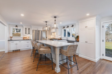 Eat-in kitchen - large country l-shaped medium tone wood floor and brown floor eat-in kitchen idea in Boston with a farmhouse sink, shaker cabinets, white cabinets, quartz countertops, white backsplash, subway tile backsplash, stainless steel appliances, an island and white countertops