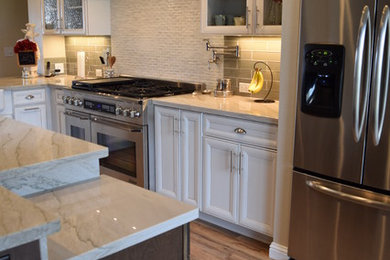 Open concept kitchen - large transitional l-shaped medium tone wood floor open concept kitchen idea in Other with recessed-panel cabinets, white cabinets, quartzite countertops, green backsplash, glass sheet backsplash, stainless steel appliances and an island