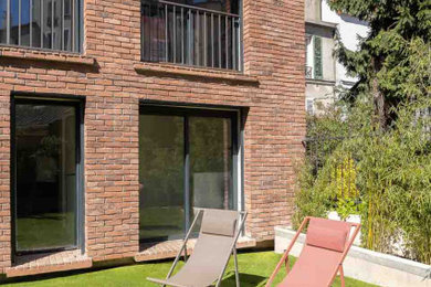 Exemple d'un grand jardin arrière moderne l'été avec une exposition ensoleillée, des pavés en brique et une clôture en métal.