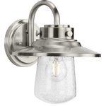 Progress Lighting - Tremont 1 Light Outdoor Wall Light, Stainless Steel - Welcome family and friends home with the Tremont Collection 1-Light Clear Seeded Glass Stainless Steel Industrial Outdoor Medium Wall Lantern Light. A light source glows from within a clear seeded glass shade reminiscent of raindrops on a window after a summer thunderstorm for a touch of rustic character. The wall light's round backplate, curved arm, and round shade decorated with mechanical fittings are coated in a stainless steel finish to accentuate the design's industrial aesthetic.