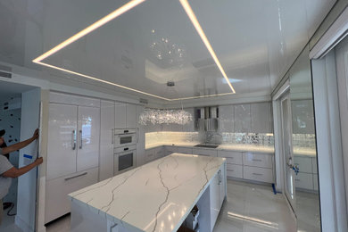 Example of a mid-sized galley wallpaper ceiling enclosed kitchen design in Miami with flat-panel cabinets, white cabinets, marble countertops, white backsplash and an island