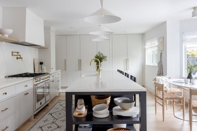 Example of a large danish l-shaped light wood floor and brown floor eat-in kitchen design in Vancouver with a farmhouse sink, flat-panel cabinets, blue cabinets, white backsplash, stainless steel appliances, an island and white countertops