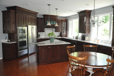 Mid-sized elegant u-shaped medium tone wood floor eat-in kitchen photo in Baltimore with a drop-in sink, raised-panel cabinets, dark wood cabinets, granite countertops, white backsplash, ceramic backsplash, stainless steel appliances and an island