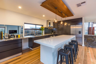 This is an example of a contemporary kitchen pantry in Canberra - Queanbeyan with a double-bowl sink, black cabinets, stainless steel benchtops, mirror splashback, stainless steel appliances, medium hardwood floors and with island.