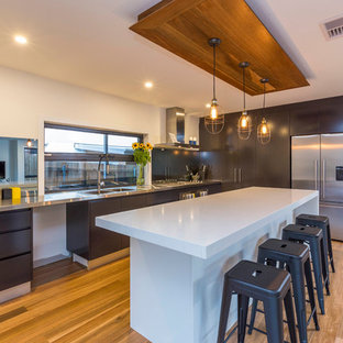 Idées déco pour une arrière-cuisine contemporaine avec un évier 2 bacs, des portes de placard noires, un plan de travail en inox, une crédence en carreau de miroir, un électroménager en acier inoxydable, un sol en bois brun et un îlot central.