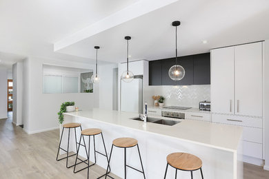 Mid-sized contemporary galley kitchen in Other with white splashback, flat-panel cabinets, ceramic splashback, light hardwood floors, white benchtop, an undermount sink, white cabinets, white appliances, with island and beige floor.