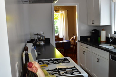 Inspiration for a mid-sized contemporary galley ceramic tile and multicolored floor eat-in kitchen remodel in Los Angeles with a single-bowl sink, shaker cabinets, white cabinets, solid surface countertops, black backsplash, quartz backsplash, stainless steel appliances, no island and black countertops