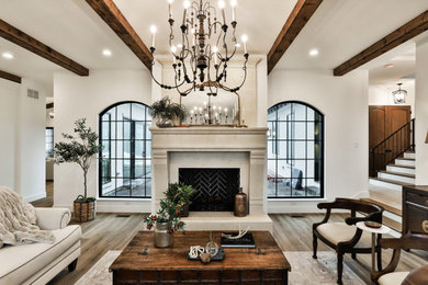 Example of a mid-sized tuscan formal and open concept medium tone wood floor, beige floor and exposed beam living room design in Other with white walls, a standard fireplace, a stone fireplace and no tv