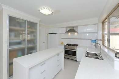 Photo of a mid-sized contemporary l-shaped eat-in kitchen in Perth with a double-bowl sink, quartz benchtops, ceramic splashback, stainless steel appliances, ceramic floors, with island and white splashback.