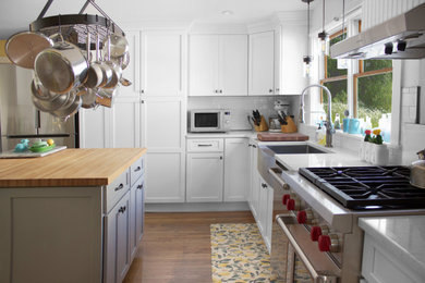 Inspiration for a mid-sized country u-shaped medium tone wood floor and brown floor eat-in kitchen remodel in New York with a farmhouse sink, recessed-panel cabinets, white cabinets, quartz countertops, white backsplash, subway tile backsplash, stainless steel appliances, an island and white countertops