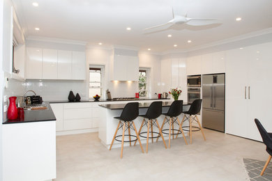 Photo of a mid-sized contemporary galley eat-in kitchen in Sydney with a double-bowl sink, white cabinets, quartz benchtops, white splashback, ceramic splashback, stainless steel appliances, ceramic floors and with island.