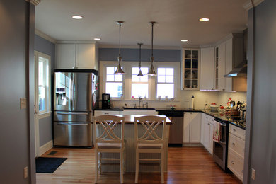 Enclosed kitchen - mid-sized traditional l-shaped medium tone wood floor and brown floor enclosed kitchen idea in Raleigh with a farmhouse sink, shaker cabinets, white cabinets, granite countertops, white backsplash, subway tile backsplash, stainless steel appliances, an island and black countertops